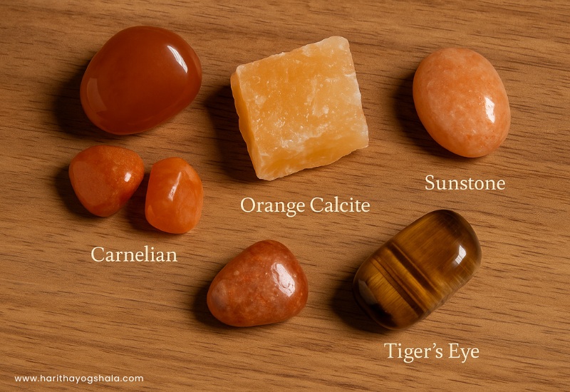 Collection of orange aura healing crystals like carnelian, sunstone, orange calcite, and tiger’s eye on wooden surface